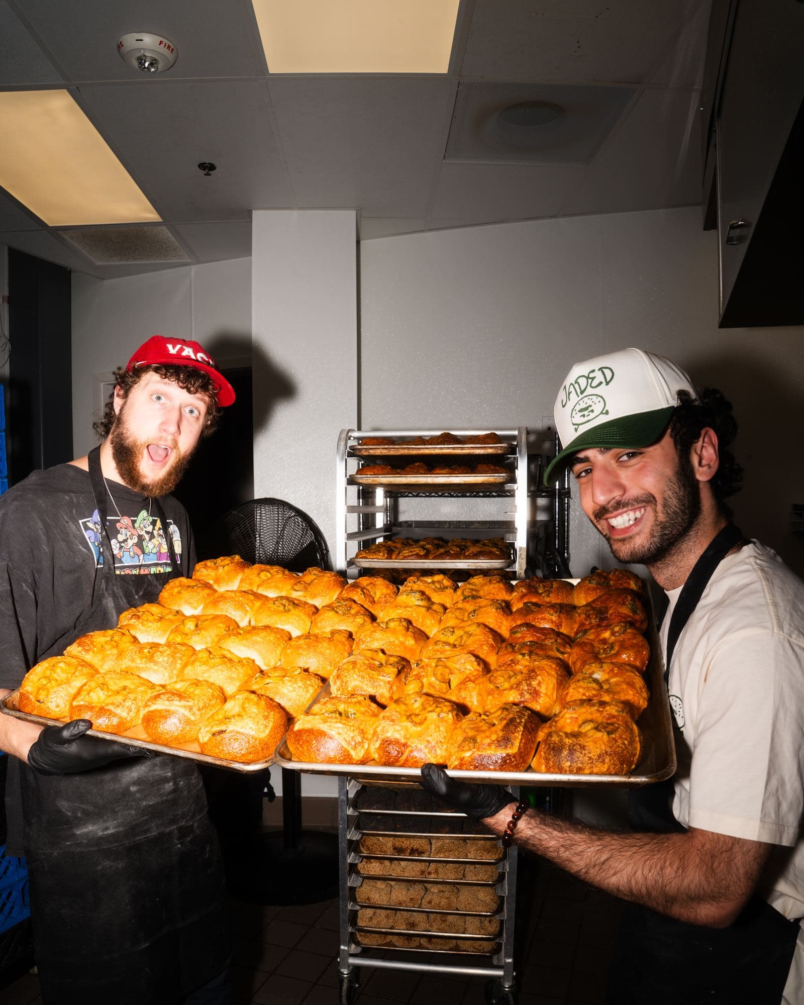 Two Jaded bakers holding up full trays of jalapeño cheddar bagels in the kitchen